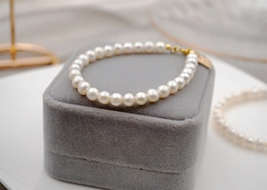 Macro view of white freshwater pearl bracelet on grey velvet with golden lobster clasp