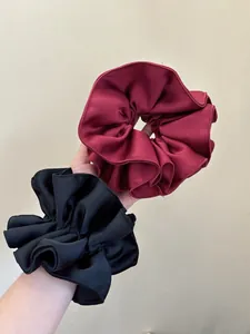 Detailed view of oversized matte scrunchies in burgundy and black with layered pleats