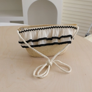 Detail of woven straw crossbody bag with white chiffon ruffle and black ribbon trim
