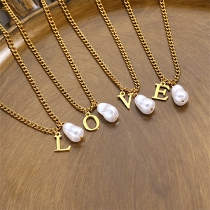 Close-up of gold LOVE letter pendants with baroque pearl charms on thin chains