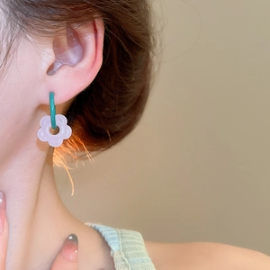 Detail of flower dangle earring with green hoop and purple petal on a model