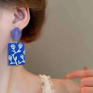 Close-up of floral drop earring with purple petal top and blue resin floral pendant