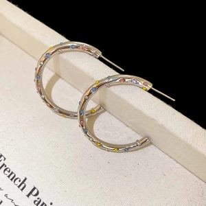 Détail de boucles d'oreilles créoles argentées en C avec cristaux colorés sur support