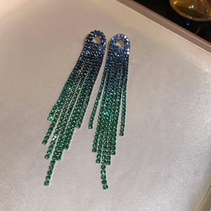 Detail of long tassel earrings with blue and green ombre rhinestones on a beige tray