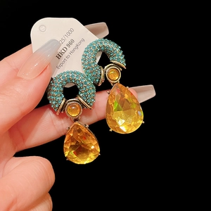 Close-up of luxury drop earrings with green pave crystals and faceted yellow gemstones