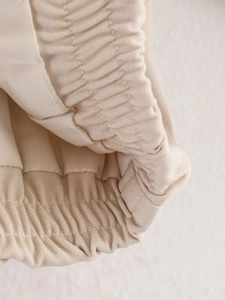 Detail of beige zip-up jacket showing elastic ruffled hem and twill fabric texture