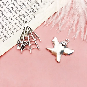 Silver Halloween spider web and ghost charms for DIY jewelry on a pink background