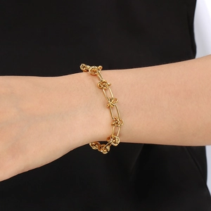 Close-up of a gold titanium steel knotted chain bracelet worn on a wrist against black silk