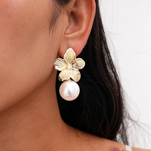 Detail of golden flower earring with large pearl and textured petals on a model