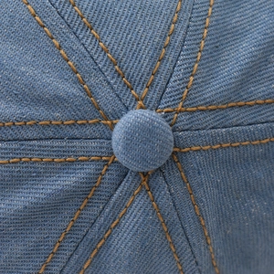 Dettaglio macro del cappello in denim con cuciture gialle e trama di tessuto blu denim