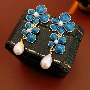 Detailed close-up of blue enamel flower earrings with gold finish and pearl pendants