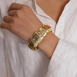 Detail of a wide gold metal cuff bracelet with irregular hammered ripple texture on wrist