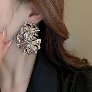 Detailed view of oversized silver floral earrings with pleated texture worn by model