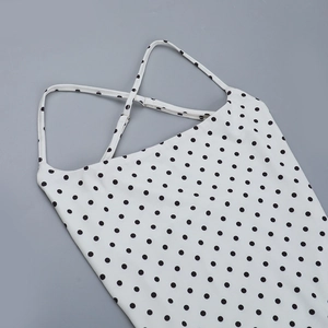 Détail d'un body blanc à pois avec fines bretelles croisées sur un fond gris clair