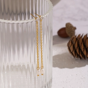 Minimalist gold chain tassel earrings with freshwater pearls on a glass rim