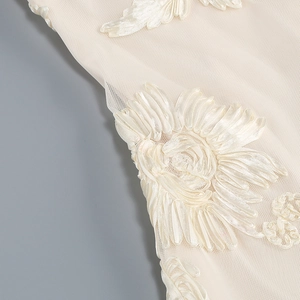 Detail of delicate white mesh fabric with elegant satin floral embroidery on evening dress