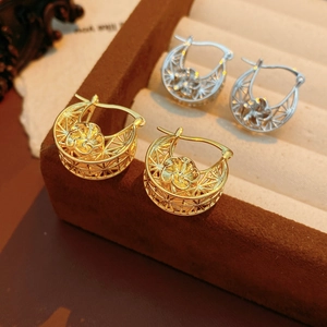 Detailed close-up of gold and silver hollow flower hoop earrings on a velvet display