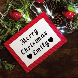 Macro view of a personalized Merry Christmas card on a rustic wooden table with pine cones