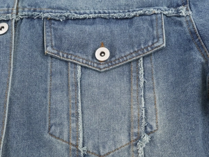 Detail of blue denim jacket showing distressed chest pocket and metal buttons