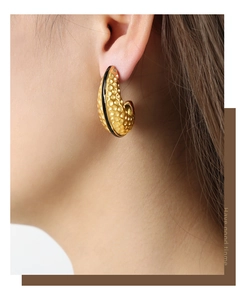 Close-up of vintage golden C-shape earrings with textured surface and black enamel inlay