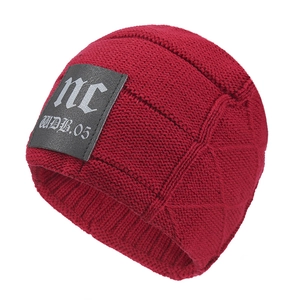 Detail of red knit beanie featuring thick vertical ribs and embossed leather logo patch