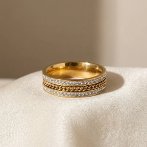Détail d'une bague large dorée avec des strass latéraux et une texture de chaîne cubaine