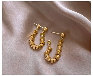 Detailed close-up of U-shaped gold beaded earrings on soft pink satin fabric