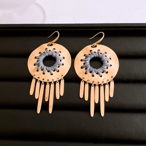 Detail of golden bohemian earrings featuring grey woven knots and metallic long tassels