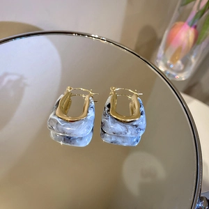 Detail of U-shaped earrings with black and white marble texture on a reflective surface