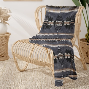 Detail of bohemian geometric pattern on soft flannel blanket draped over a wicker chair