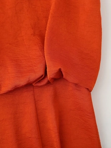 Detailed macro shot of orange satin fabric showing smooth texture and sleeve seam