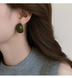 Gros plan d'une boucle d'oreille ovale en résine vert foncé sur l'oreille d'un mannequin