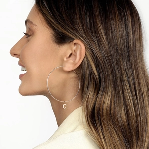 Close-up of large gold hoop earring with a crystal-encrusted letter C pendant on model