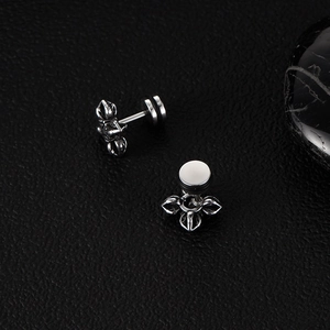 Macro shot of retro silver Vajra cross stud earrings on a textured black background