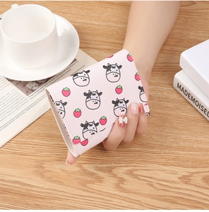 Pink tri-fold wallet featuring cow and strawberry prints held over a wooden table