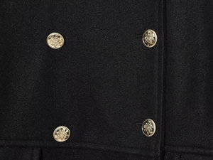 Close-up of golden embossed metal buttons on a black wool blend double-breasted coat