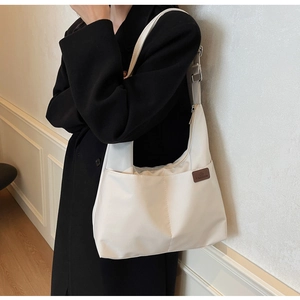 Detail of white canvas tote bag featuring brown leather patch and side pocket on the strap