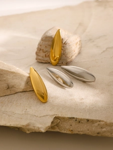 Detailed view of teardrop earrings in gold and silver finish on natural beige rock