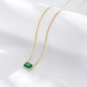 Detail of s925 silver necklace with square emerald green gem in four-prong gold setting
