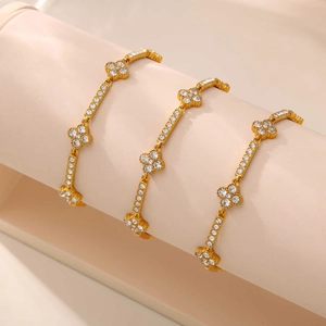 Detailed shot of three gold clover bracelets with zircon stones on a cylindrical display stand