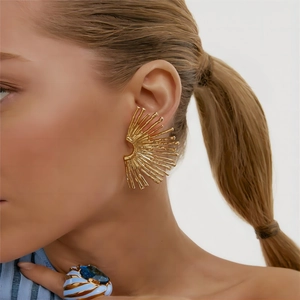 Detail of gold-plated sunburst earrings worn on ear showing ray-shaped geometric design