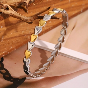 Macro detail of 18K gold and silver heart-shaped linked bracelet on a wooden stand