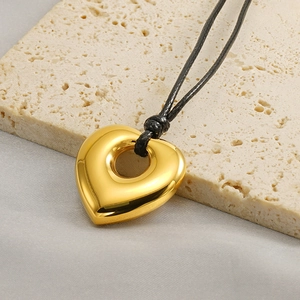 Detailed shot of hollow heart pendant on black cord over beige travertine stone
