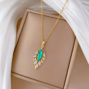 Gold necklace with emerald leaf pendant and zircon accents on a beige jewelry box