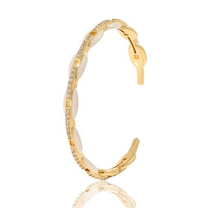Detailed close-up of a gold-plated open bangle with white enamel and sparkling rhinestones