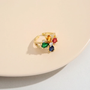 Dettaglio dell'anello a fiore dorato con zirconi colorati su un piedistallo bianco