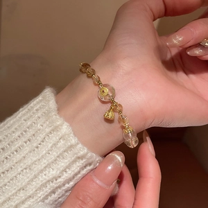 Detailed view of yellow quartz beaded bracelet with gold bell charm on a female wrist