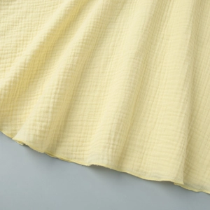Detail of yellow cotton mini dress fabric showing light waffle texture and hem stitching