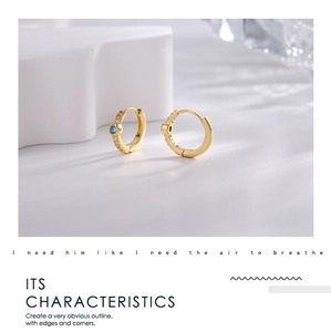 Close-up of golden hoop earrings with central blue zircon and white sparkling accents