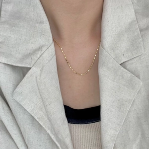 Close-up of a minimalist gold rectangle link chain necklace worn on a grey linen blazer